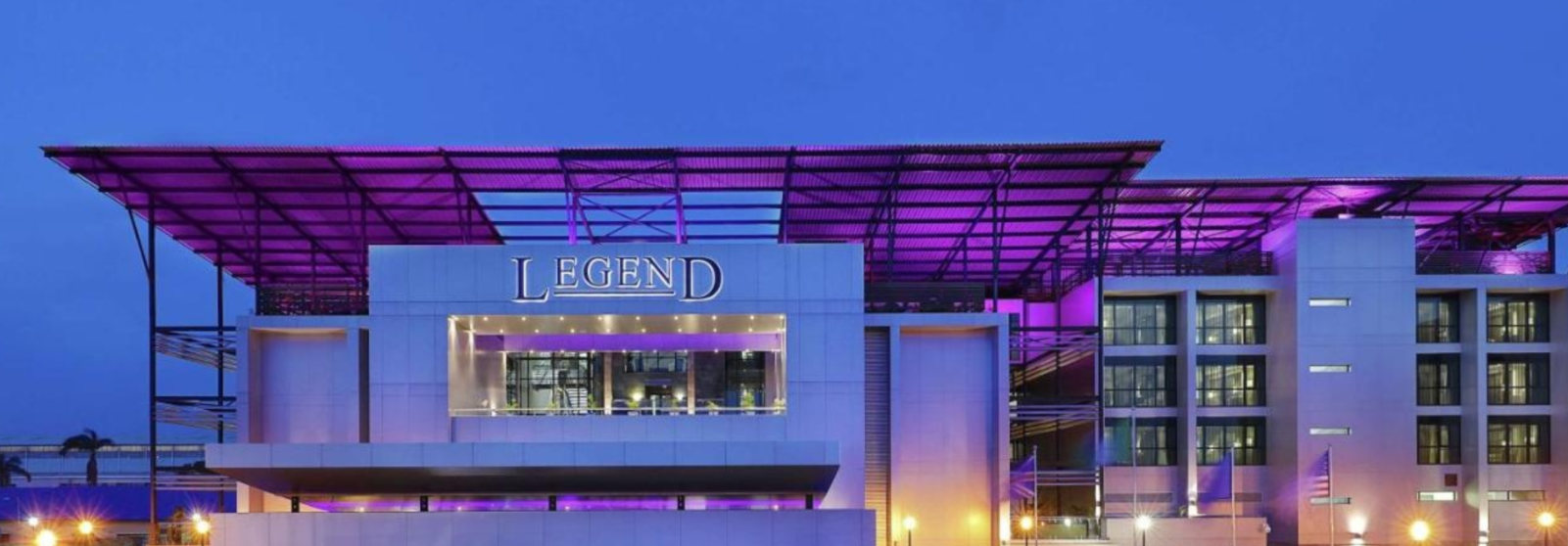 The purple-lit canopy and facade of Legend Hotel, Curio Collection by Hilton, at night
