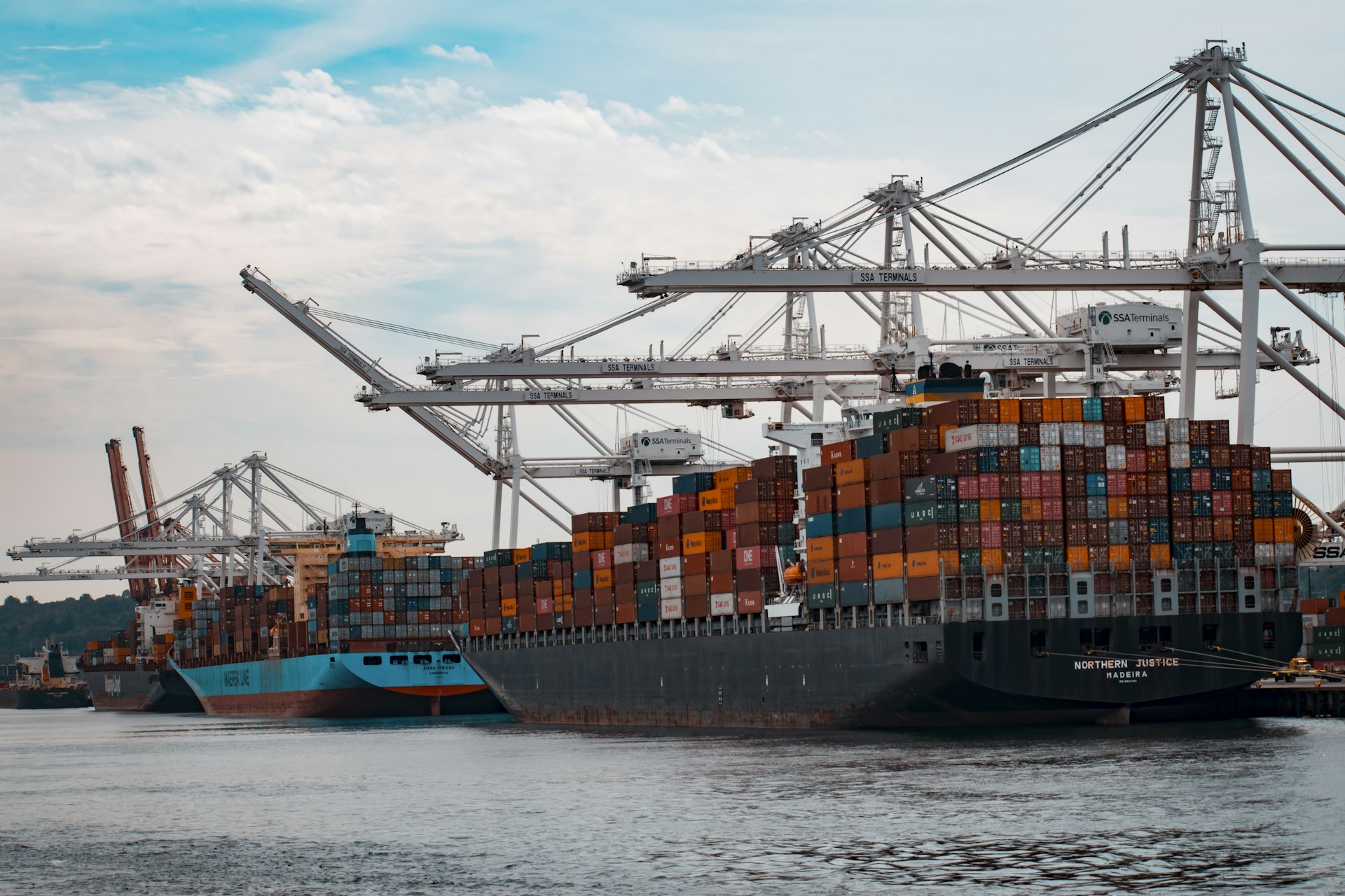 A container ship loaded with shipping containers being worked by gantry cranes at port