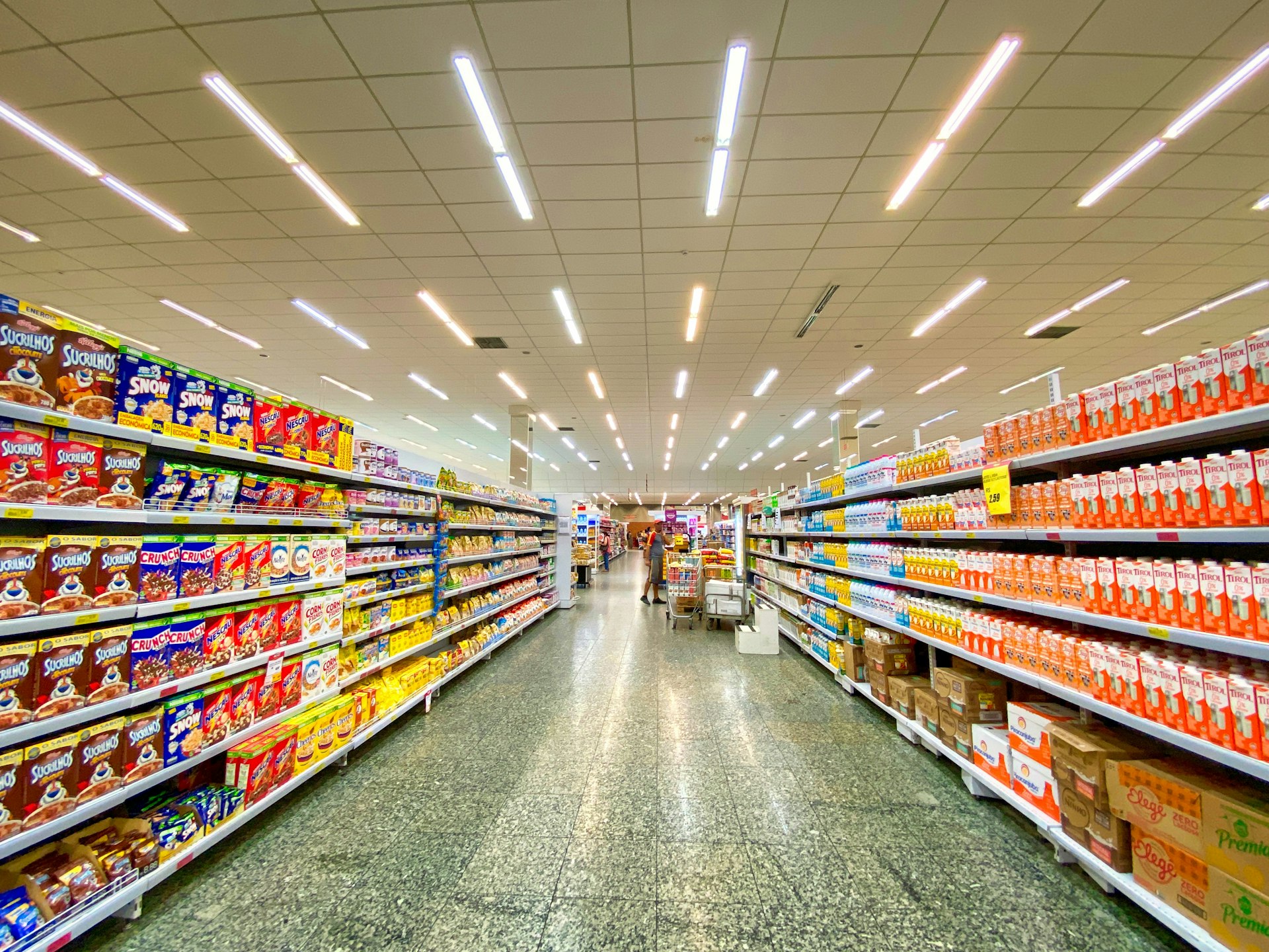 A bright, well-stocked supermarket aisle viewed down its full length